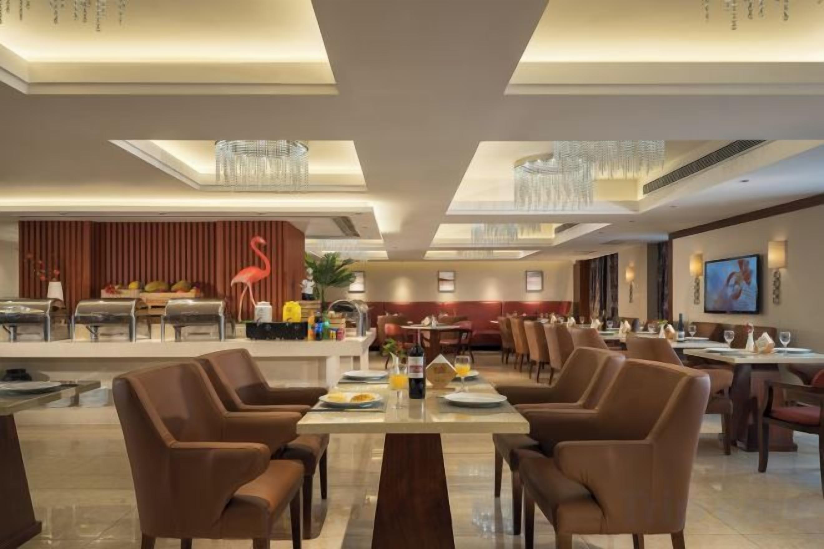 A hotel dining area with multiple tables and chairs, a reception desk, and a television screen.