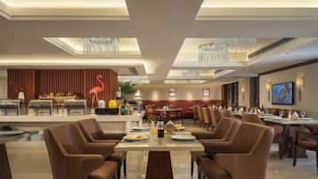 A hotel dining area with multiple tables and chairs, a reception desk, and a television screen.