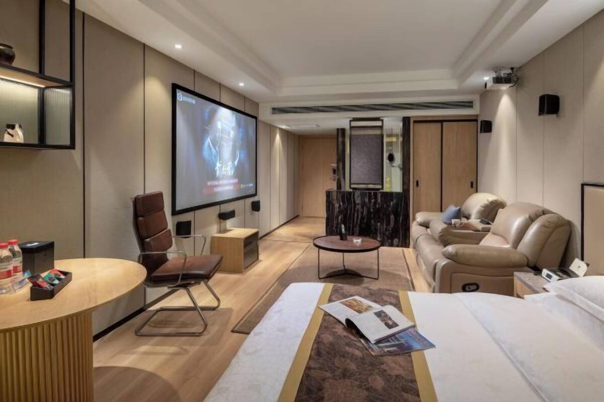 A modern hotel room with a flat-screen TV, a sofa, a recliner, a small table, and a bed.