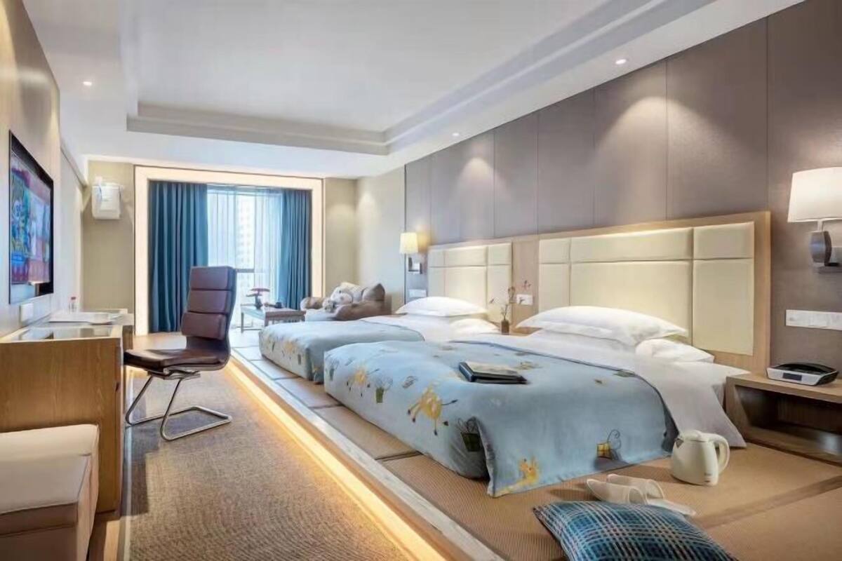A hotel room with two beds, a desk, a chair, a TV, and a window with curtains.
