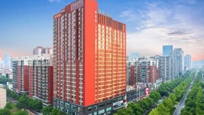 A high-rise hotel with a red facade, surrounded by other buildings and a tree-lined street. - Ming Yi Hotel (Zhuzhou)