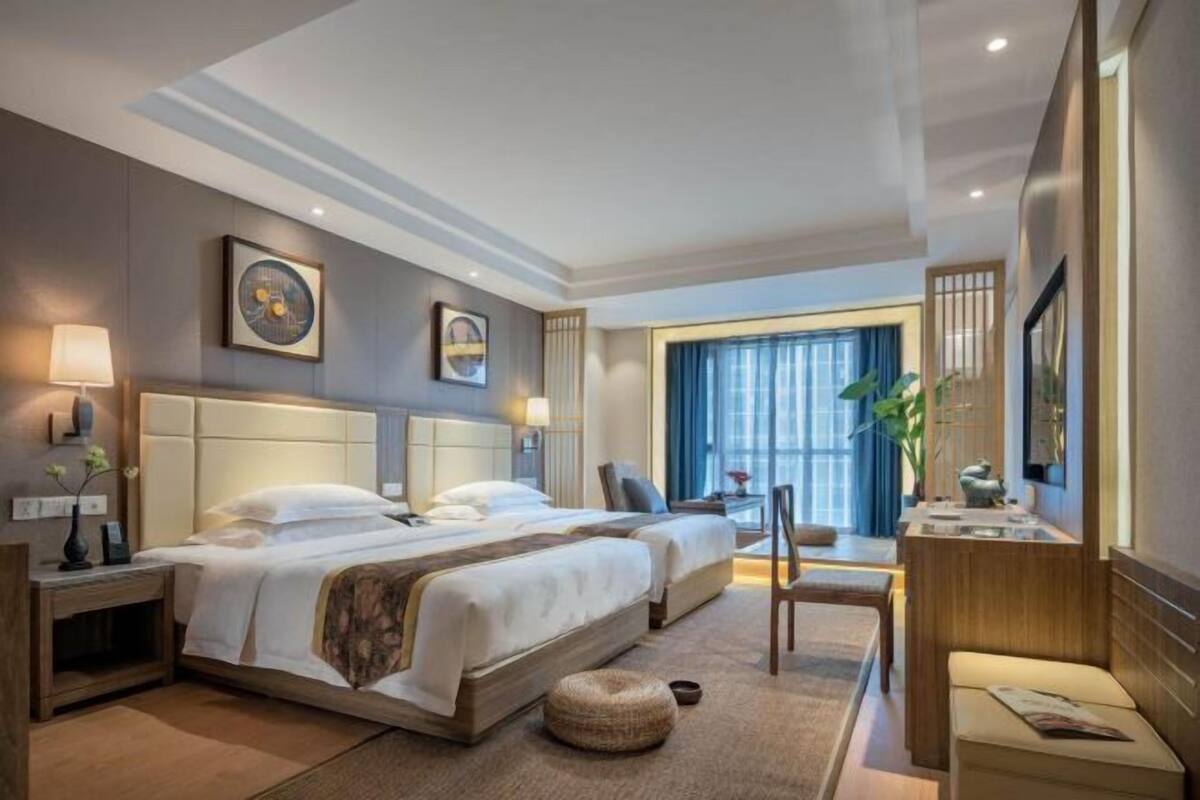 A hotel room with two beds, a sitting area, a desk, and a large window with curtains.