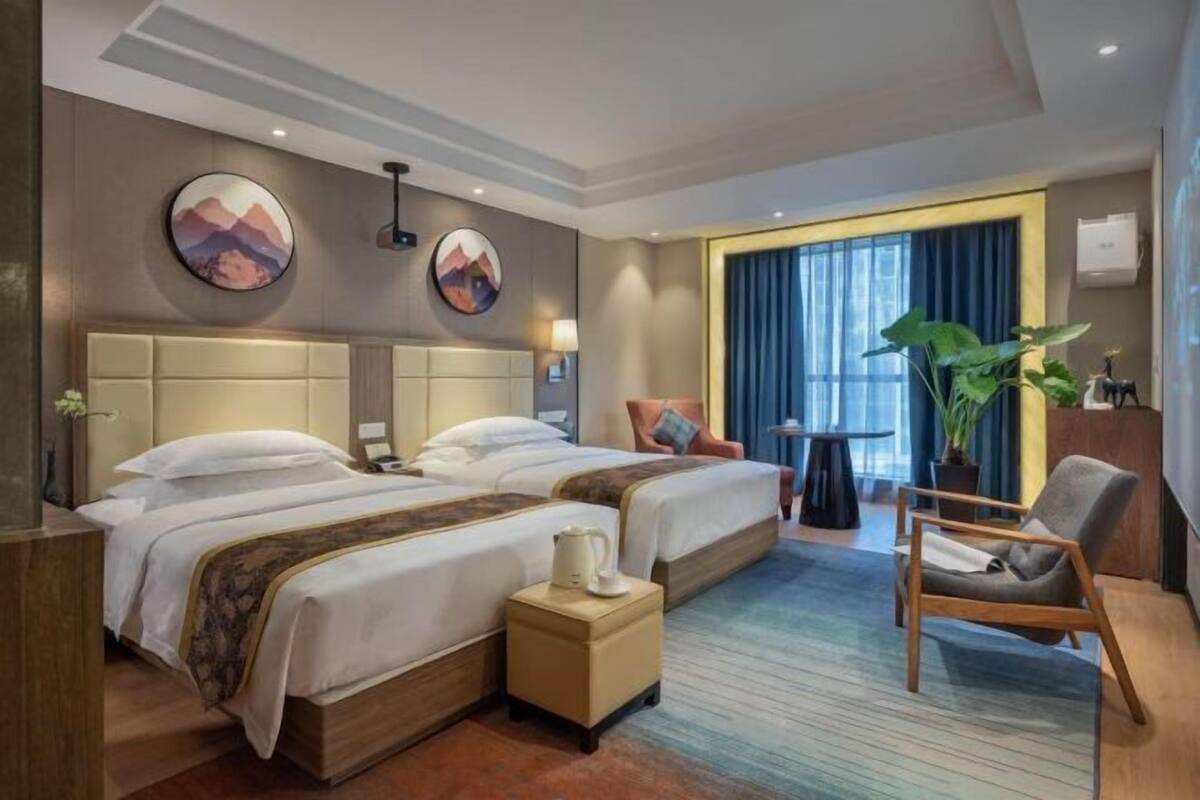A hotel room with two beds, a seating area, a small table, and a large window.