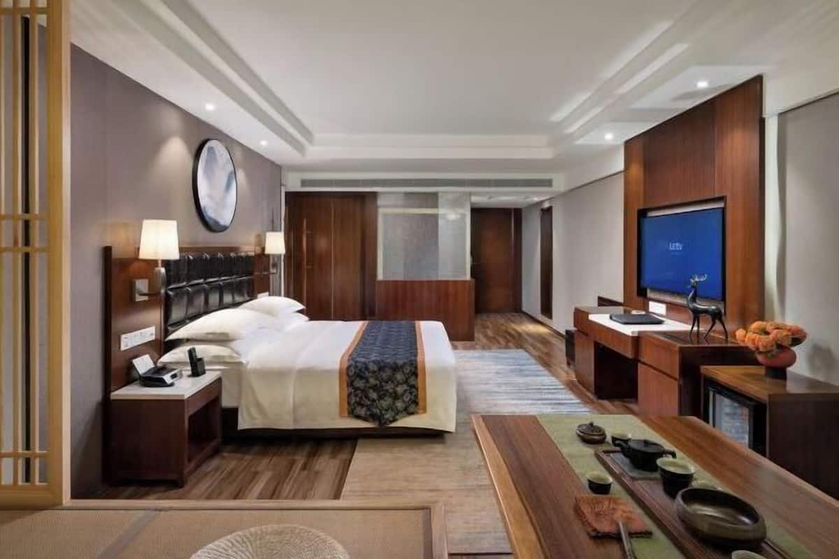A hotel room with a bed, bedside table, lamp, TV, and a desk with a chair.