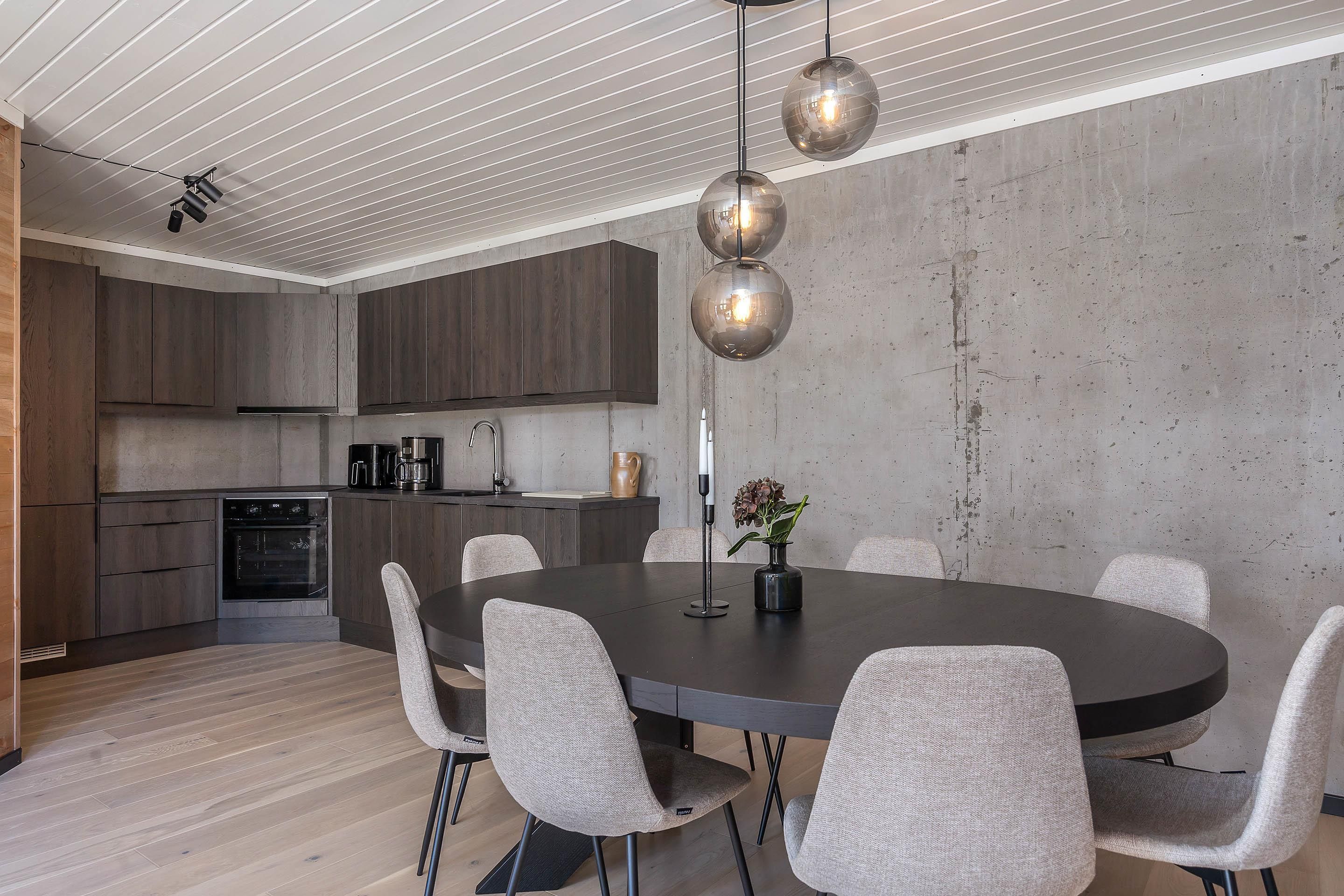 A modern kitchen with dark wooden cabinets, a round dining table with six chairs, and pendant lighting.