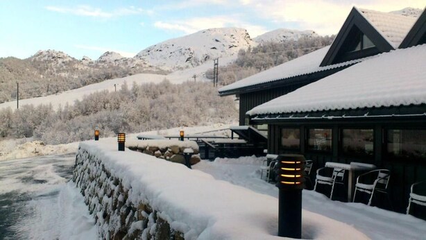 Un bâtiment enneigé doté d’une terrasse et offrant une vue sur des montagnes recouvertes de neige.