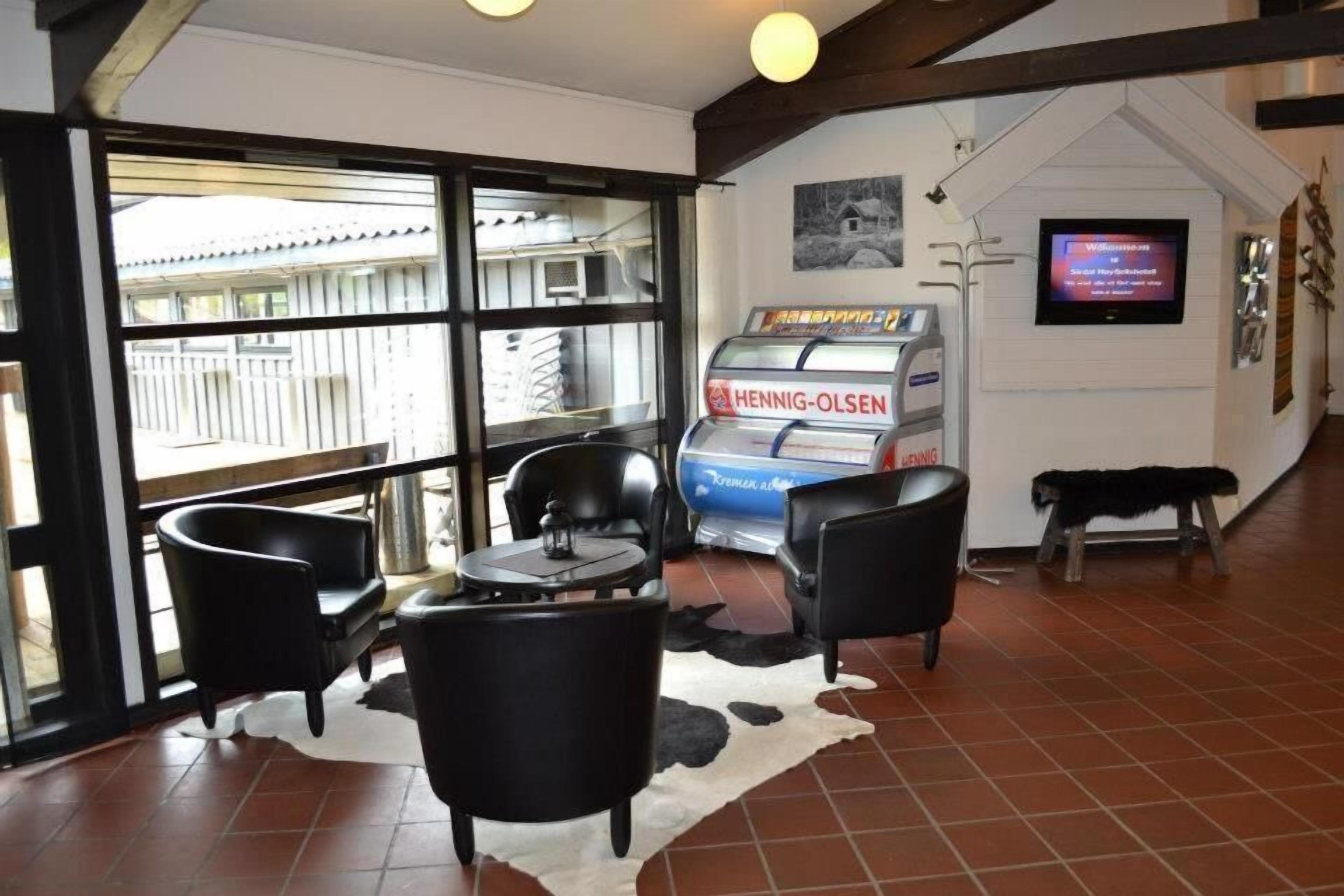 Um quarto com porta de vidro que dá para o exterior, uma televisão fixada na parede e uma máquina de vendas automática com a inscrição "Hennig-Olsen".