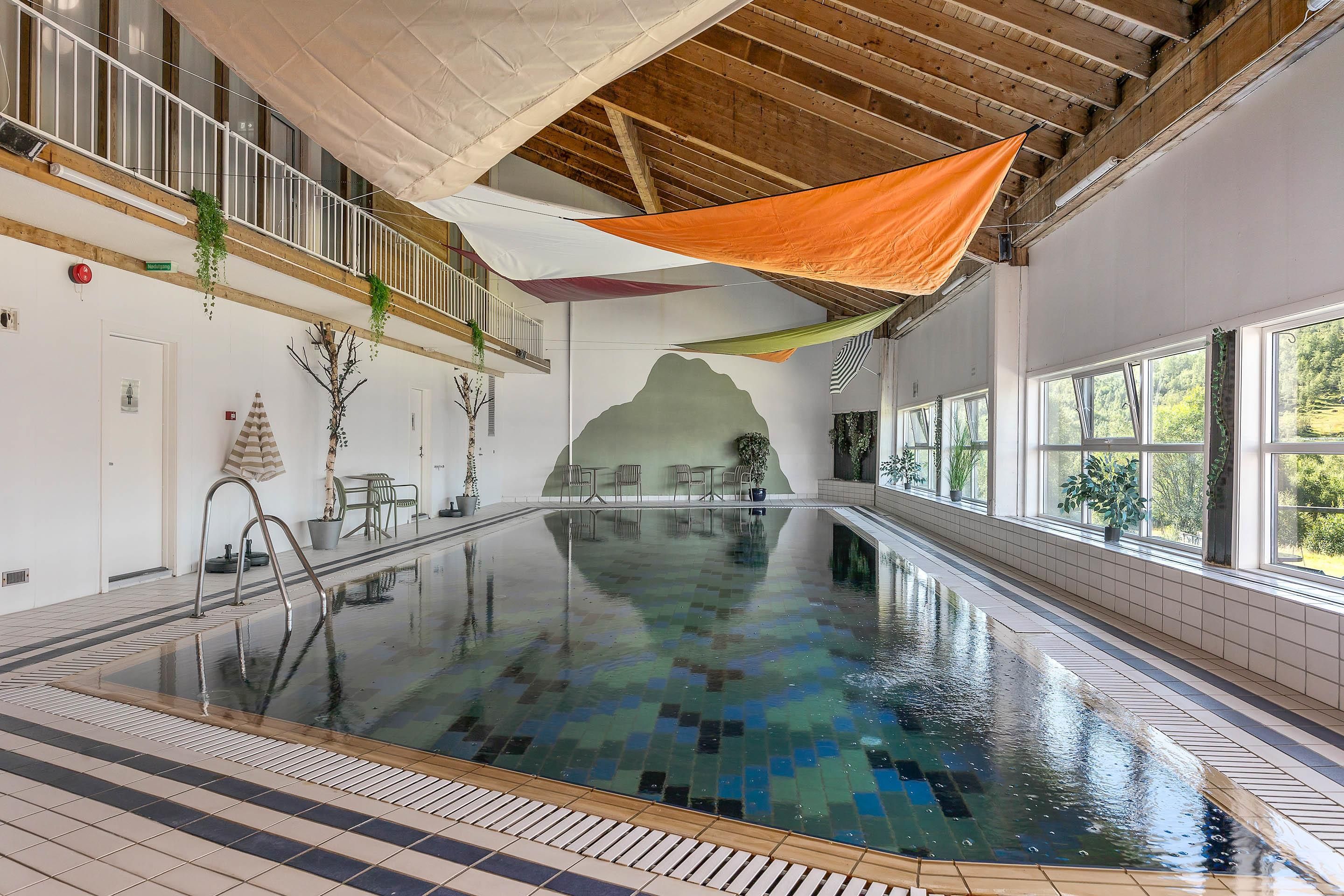 Piscina interna com chão em azulejo, plataforma de salto e vista para o exterior através de grandes janelas.