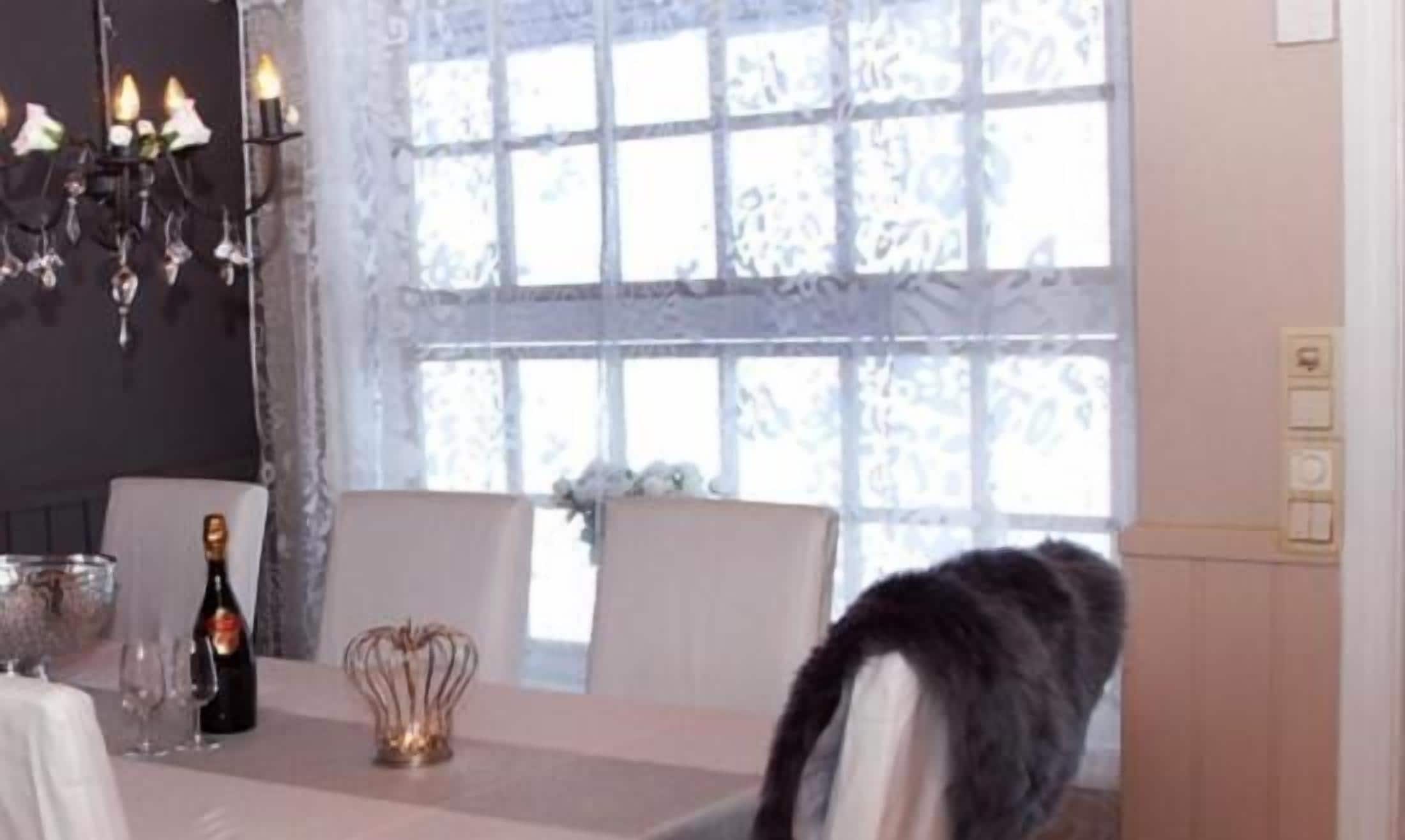 Un comedor con una mesa lista para dos personas, un candelabro y un ventanal con cortinas estampadas.