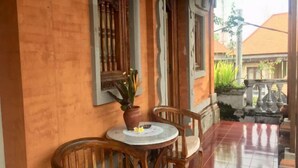 Una mesa de madera con sillas sobre un piso de baldosas, una planta en maceta y un ventanal con detalles de madera decorativa.