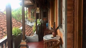 Un espacio exterior techado con un banco de madera, plantas en macetas y un techo de baldosas al fondo.