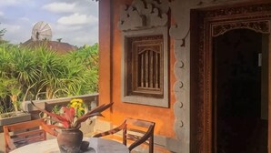Una terraza con una mesa y sillas, una planta en maceta y un ventanal con marco decorativo.
