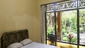 Una cama con cabecera, una ventana con vistas a la vegetación y una cortina.