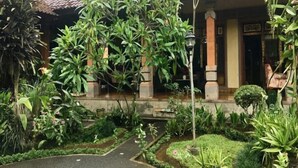 Un edificio tradicional con tejado de baldosas y un jardín con diversas plantas y un sendero.