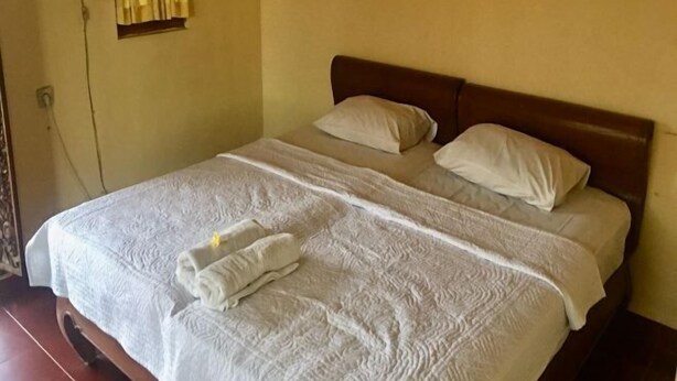 Una cama bien hecha con sábanas blancas y dos almohadas, una lámpara de noche y una ventana con cortinas amarillas.