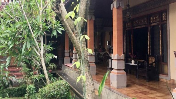 Un edificio tradicional con suelo de baldosas, un acceso cubierto con columnas y un pequeño espacio al aire libre con mesas y sillas.