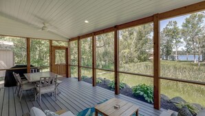 A covered outdoor deck with wooden furniture, a table, and a view of a lake and forest. - Big Pine Beach House (Crosslake)