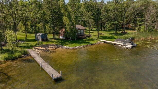 A lakeside property with a dock, a small cabin, and a larger house surrounded by trees. - Big Pine Beach House (Crosslake)