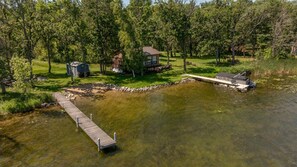 A lakeside property with a dock, a small cabin, and a larger house surrounded by trees. - Big Pine Beach House (Crosslake)