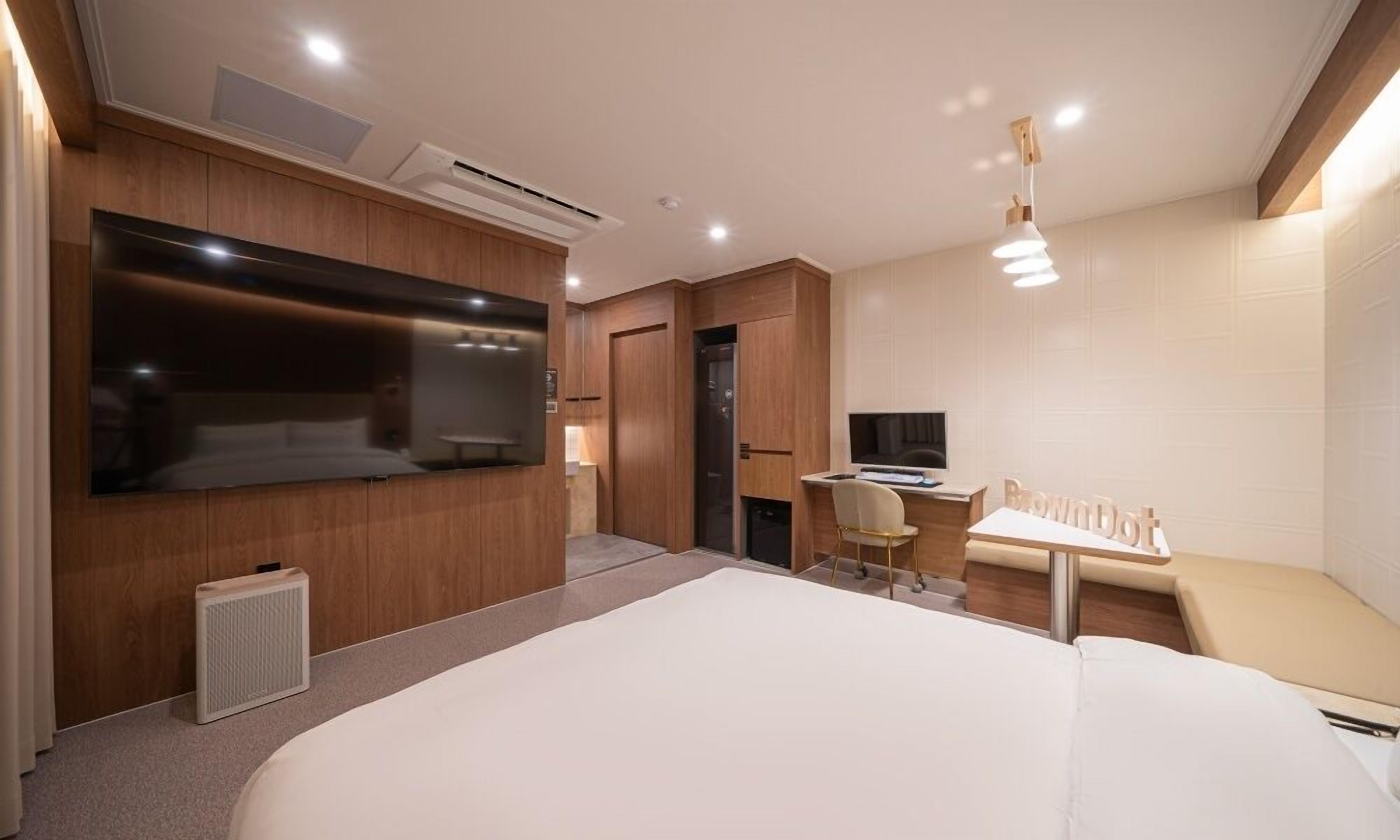 A modern hotel room with a large bed, a desk, a television, and a wardrobe.