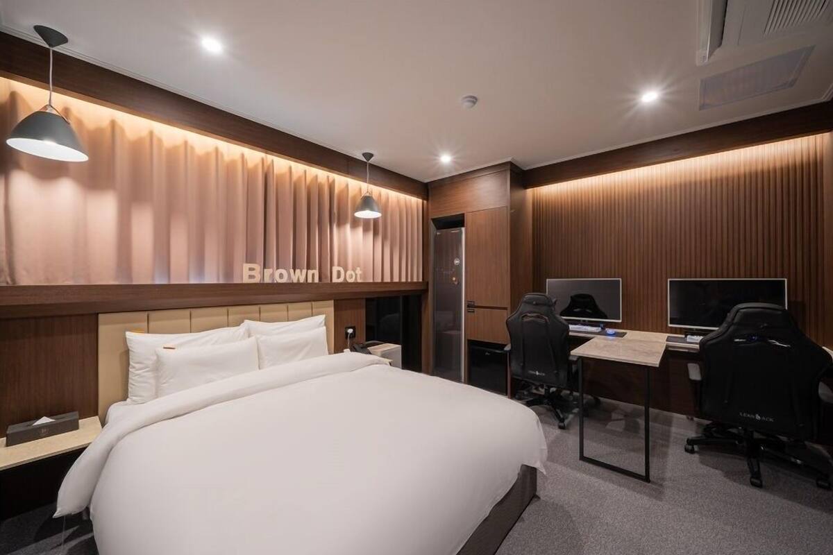 Ein Hotelzimmer mit einem großen Bett, einem Schreibtisch mit zwei Bildschirmen, einem Stuhl und einem Kleiderschrank.