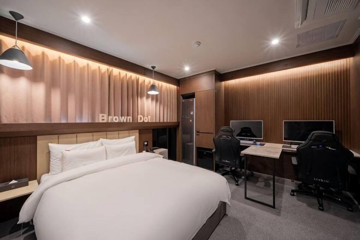 Ein Hotelzimmer mit einem großen Bett, einem Schreibtisch mit zwei Bildschirmen und einem Gaming-Sessel.