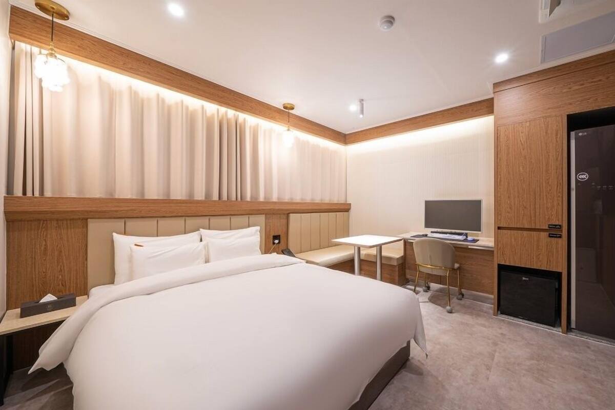 Ein Hotelzimmer mit einem großen Bett, einem Schreibtisch mit Computer und einem Kleiderschrank.