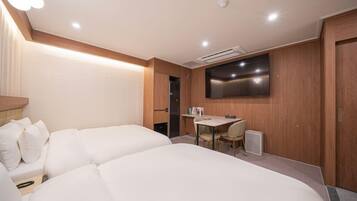 A hotel room with two beds, a desk, a chair, a flat-screen TV mounted on the wall, and a door.