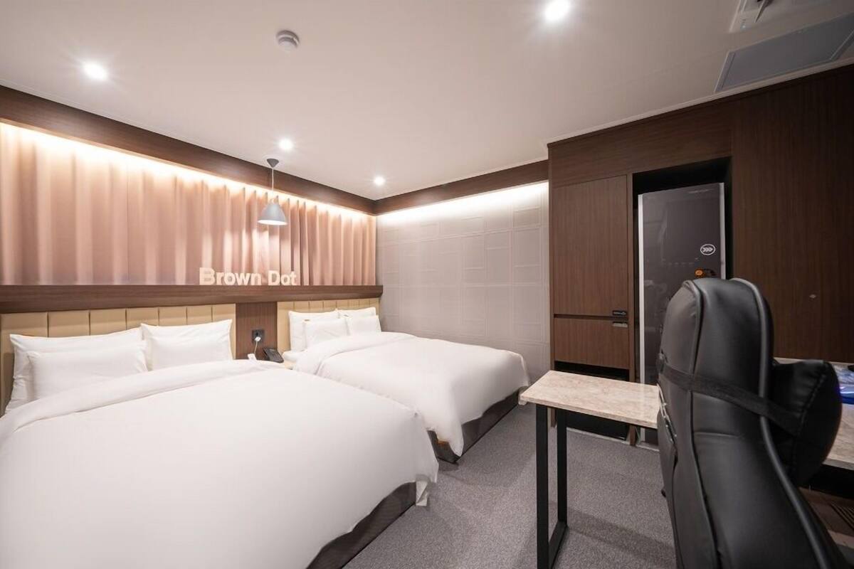 Ein Hotelzimmer mit zwei Betten, einem Schreibtisch, einem Stuhl und einem Kleiderschrank.