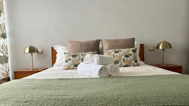 A neatly made bed with a green blanket, two bedside lamps, and floral-patterned pillows. - Casa Tuttomondo in Pisa (Pisa)