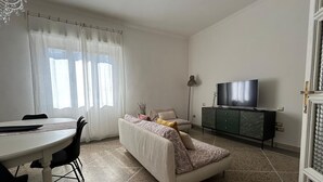 A living room with a sofa, a TV, a dining table with chairs, and a chandelier. - Casa Tuttomondo in Pisa (Pisa)