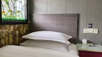 Quarto de hotel com cama, mesa de cabeceira, tomada na parede e janela com vista para plantas.