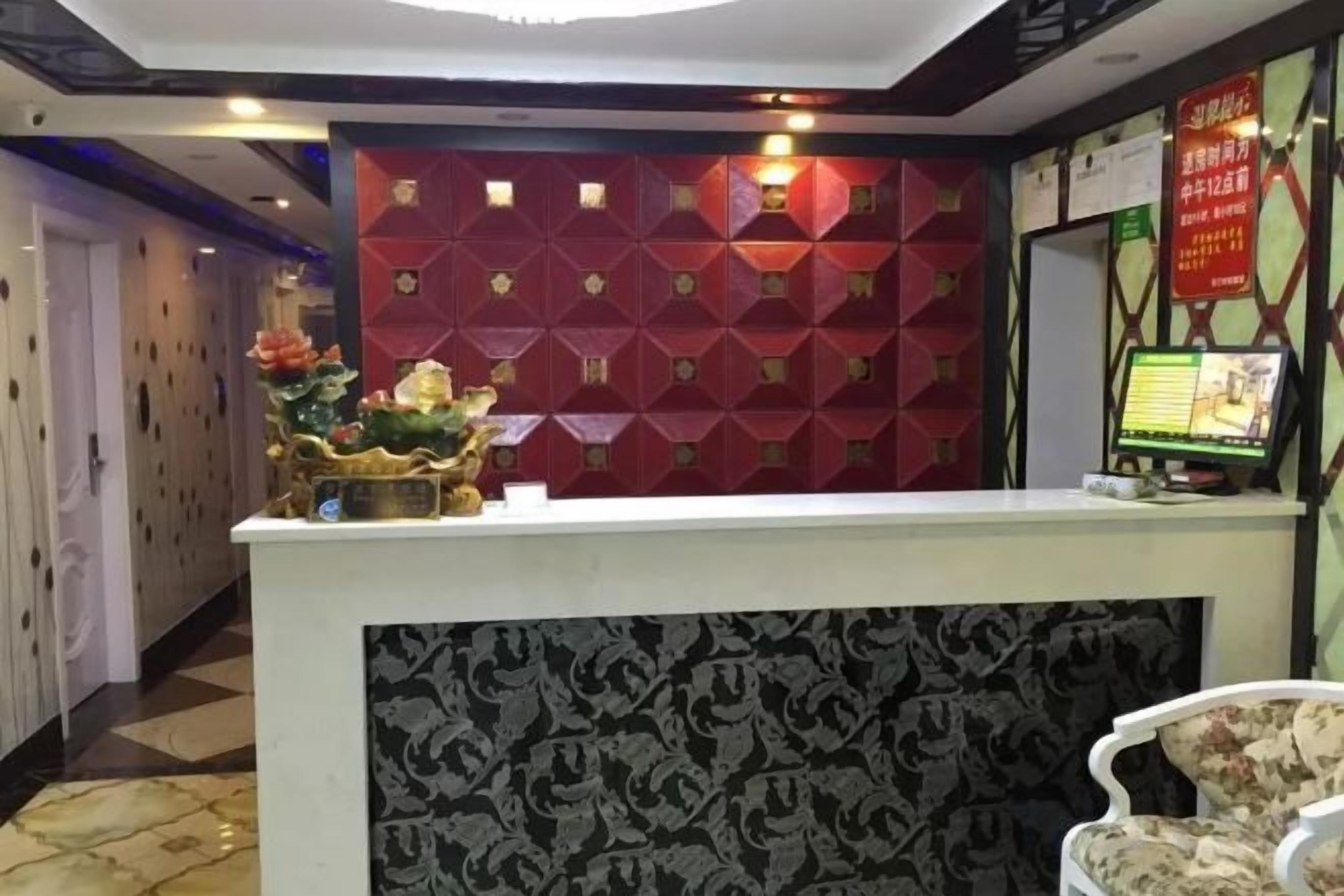 A hotel reception area with a reception desk, a decorative wall, and a digital screen displaying information.