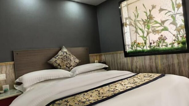A hotel room with a large bed, a nightstand, a window with a floral view, and a dark wall. - Yueyi Hotel (Shanghai)