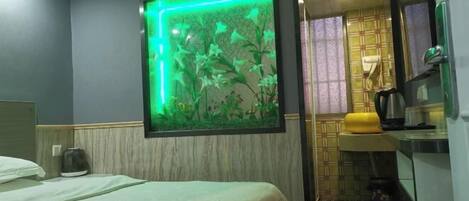 A hotel room with a bed, a wall-mounted aquarium, a sink, and a mirror.