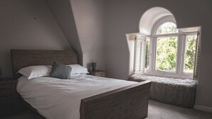 Ein Schlafzimmer mit einem hölzernen Bett, einem Nachttisch, einer Lampe und einem Fenster mit Blick auf Bäume.