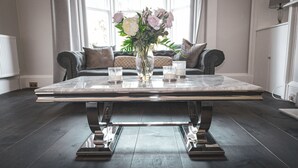Ein moderner Esstisch mit Blumen in einer Vase und Kerzen in einem Raum mit dunklem Holzboden, einer Couch und großen Fenstern.