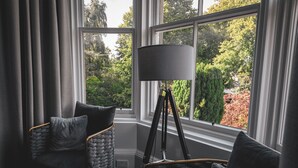 A room with a corner sofa, a floor lamp, and a view of a garden through large windows. - Beautiful Apartment in Stirling (Stirling)