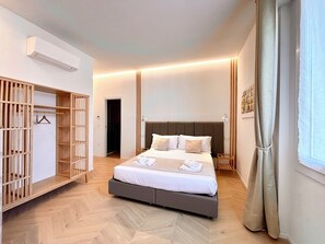 A modern bedroom with a large bed, a walk-in closet, and a view of the city through a window. - Reno Suite Bologna (Bologna)
