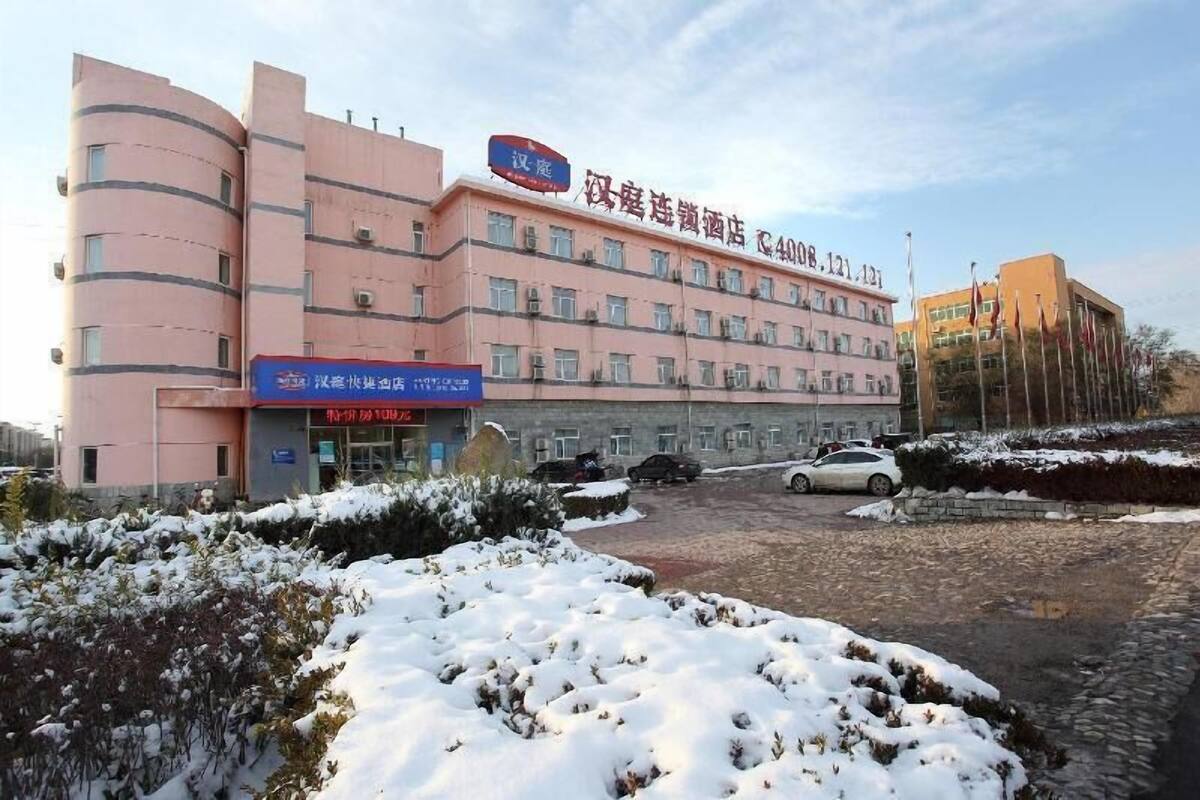 Een hotel met meerdere verdiepingen, een roze gevel, een parkeerplaats en een met sneeuw bedekte grond.