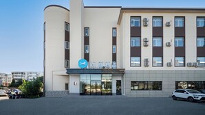 Ein modernes Gebäude mit einem Schild, auf dem '汉庭酒店' (Han Tian Hotel) steht. Es hat eine geschwungene Fassade, zahlreiche Fenster und Klimaanlagen.