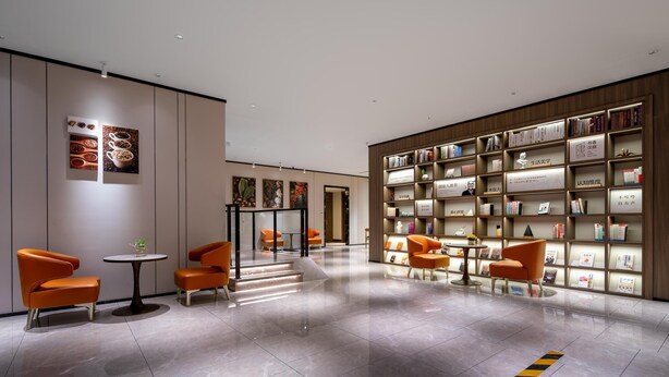 Eine moderne Lobby mit einer zentralen Treppe, orangefarbenen Sitzgelegenheiten und einem großen Bücherregal.
