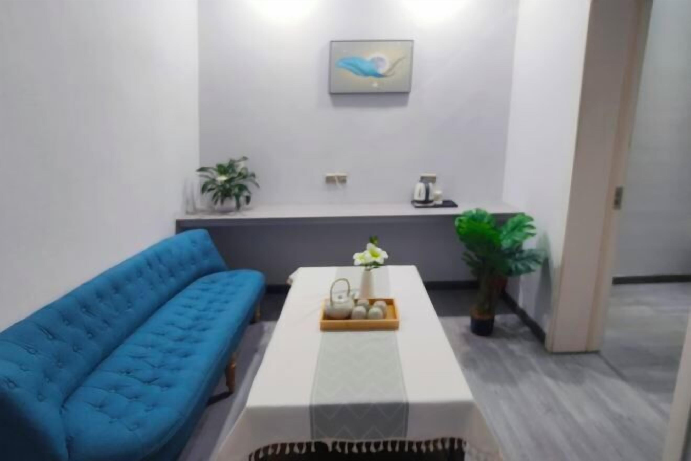 A modern living room with a blue sofa, a white coffee table with a tray of items, a potted plant, and a wall-mounted artwork.