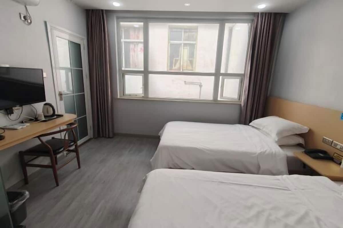 Une chambre d’hôtel avec deux lits, un bureau avec une télévision et une fenêtre avec des rideaux.