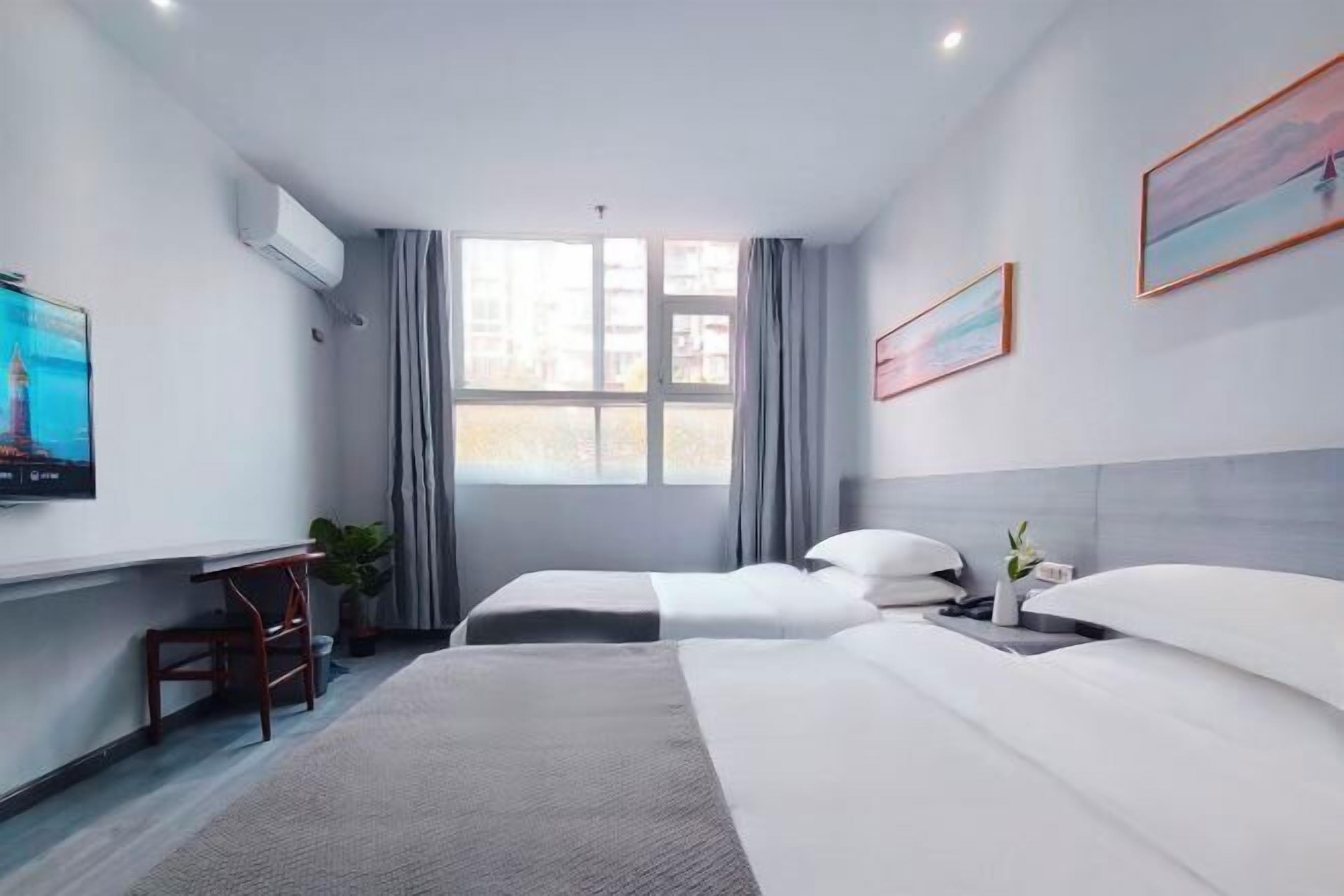 A hotel room with two beds, a desk, a TV, and a window with curtains.