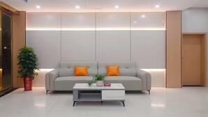 Eine moderne Hotelhalle mit neutralen Farben, einem Sofa mit orangefarbenen Kissen, einem weißen Couchtisch und einer Topfpflanze.