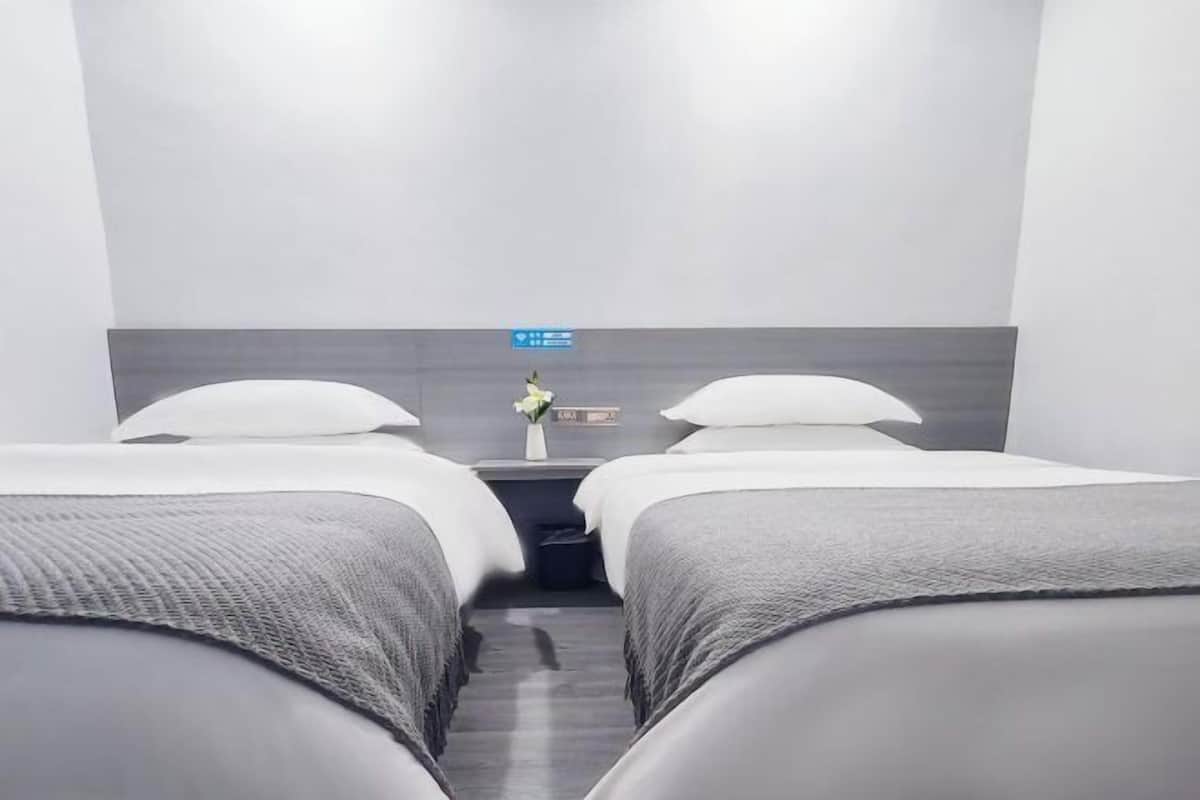 Une chambre d’hôtel avec deux lits simples, une table de chevet ornée d’un vase de fleurs et un panneau de commande fixé au mur.