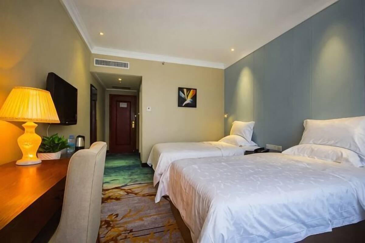A hotel room with two beds, a desk with a lamp, a television, and a door leading to another room.