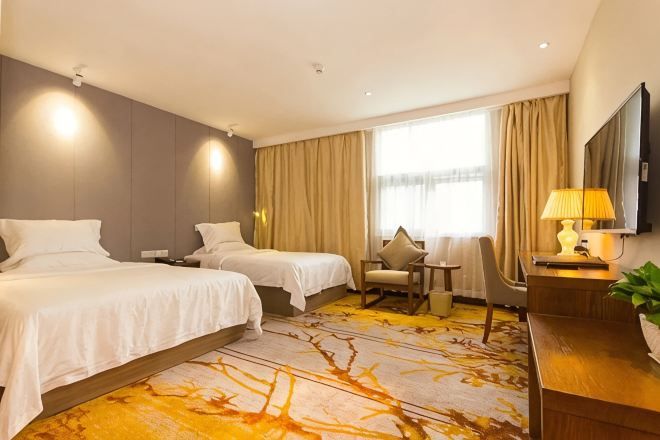 A hotel room with two beds, a desk, a chair, a TV, and a window with curtains.
