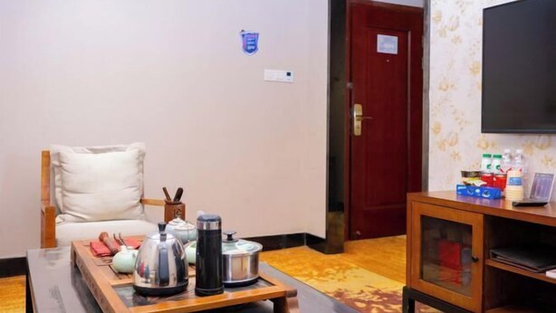 A room with a wooden coffee table, a white chair, a television on a stand, and a cabinet with various items. - Dongfang Yuehai Hotel (Zhengzhou)